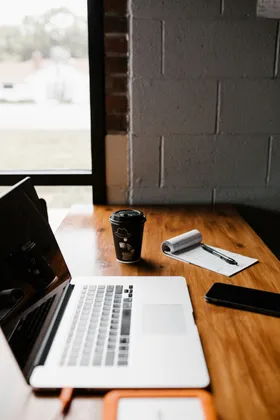 Laptop and notebook on a wooden desk near a window